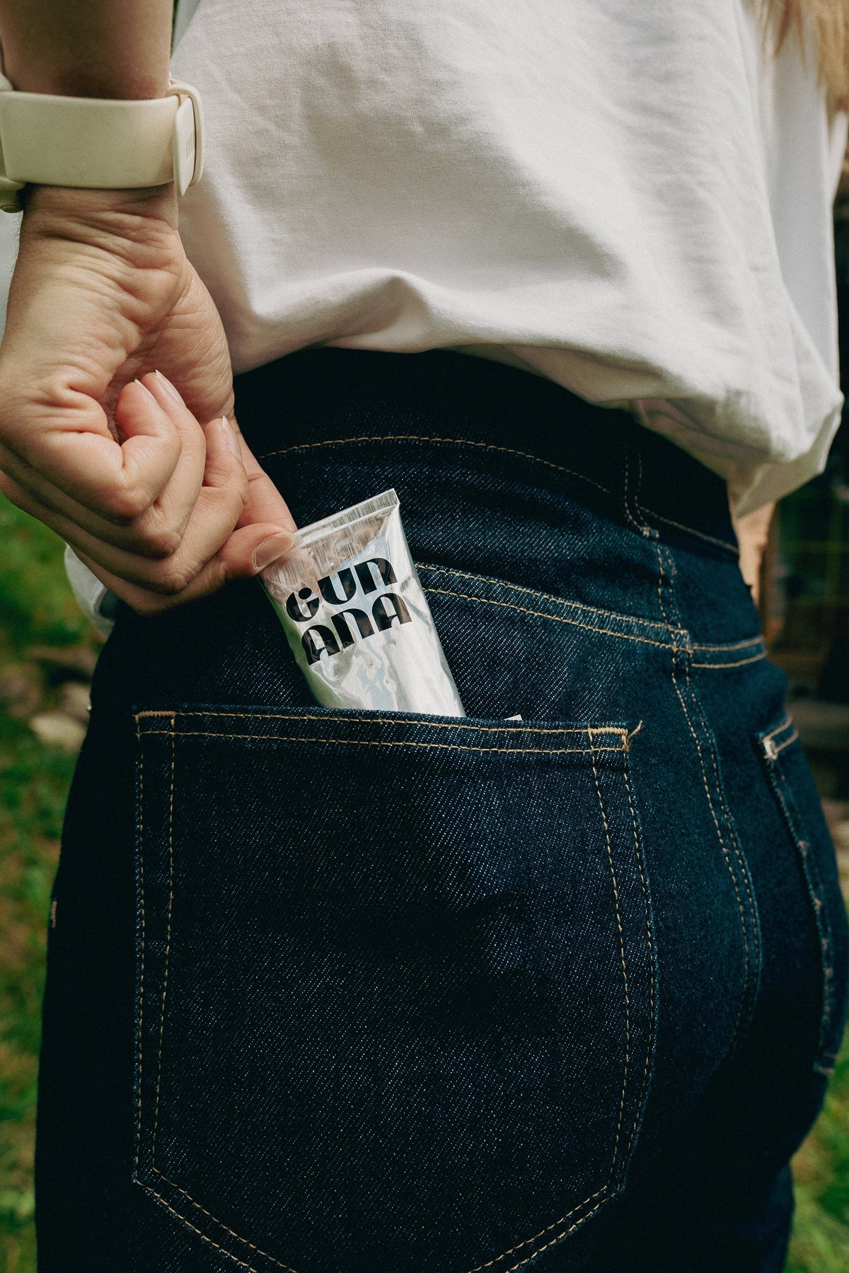 Hand placing a silver Gun Ana skincare tube in a jeans pocket